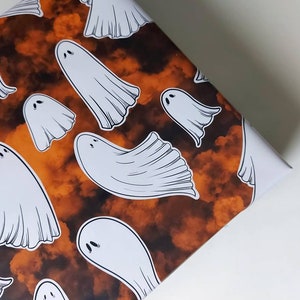 May include: Orange and brown wrapping paper with a repeating pattern of white ghosts. The ghosts are in various sizes and positions.