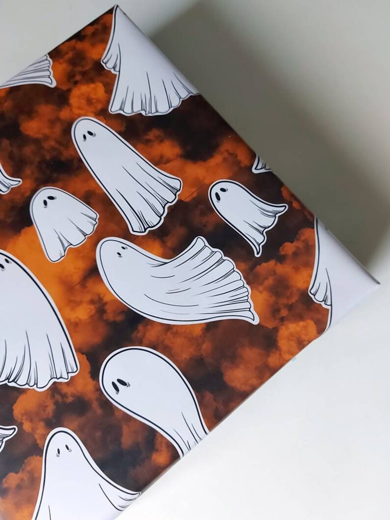 May include: Orange and brown wrapping paper with a repeating pattern of white ghosts. The ghosts are in various sizes and positions.