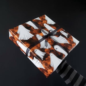 May include: Orange and white gift wrap with a pattern of ghosts flying against a cloudy background. The gift is tied with a black ribbon.