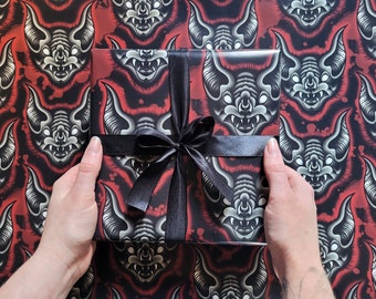 May include: A black and red gift wrap with a repeating pattern of white bat faces. A black ribbon is tied around the gift box.