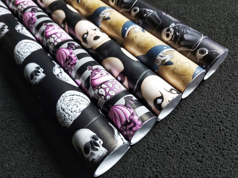 May include: A set of six black and white wrapping paper rolls with various spooky and whimsical designs. The designs include skulls, brains, cupcakes, and a ghost.