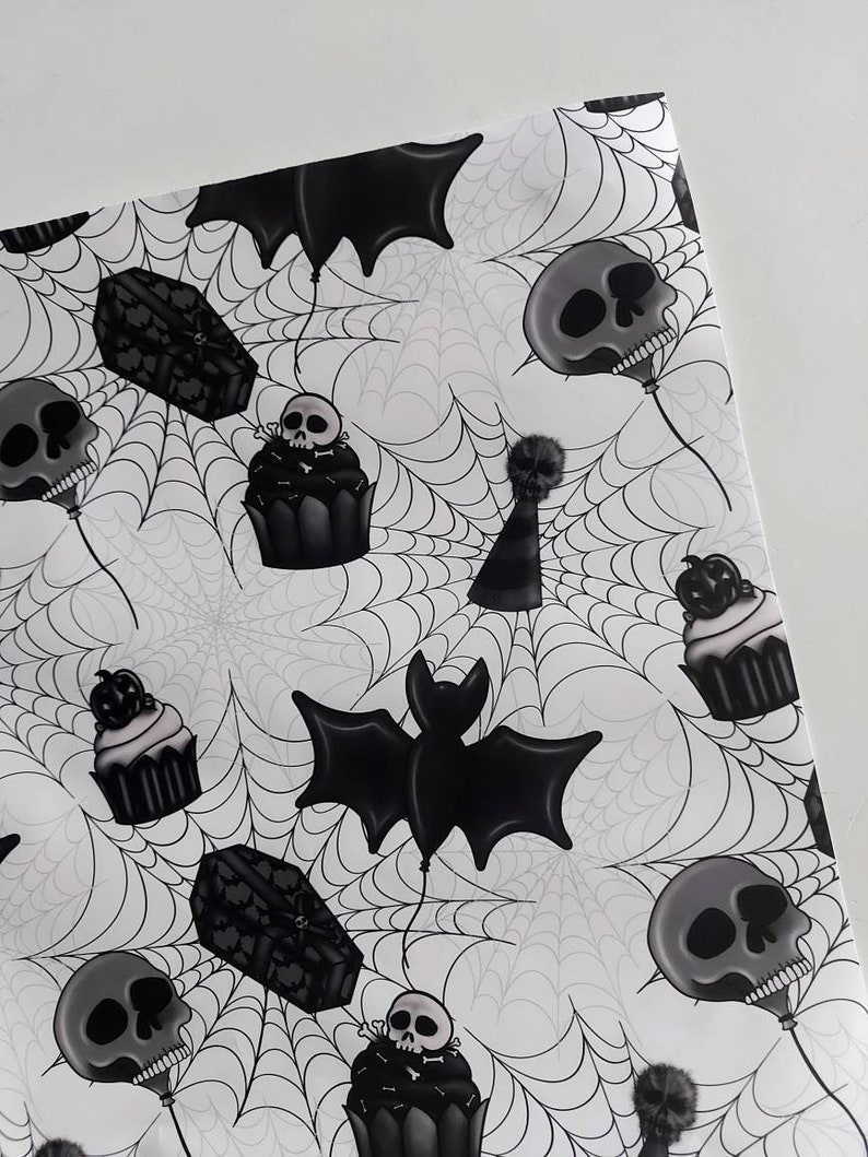 Peut inclure: Papier d'emballage sur le th&egrave;me d'Halloween noir et blanc avec un motif r&eacute;p&eacute;t&eacute; de cupcakes, de chauves-souris, de cercueils et de cr&acirc;nes. Le fond est un motif de toile d'araign&eacute;e blanche.