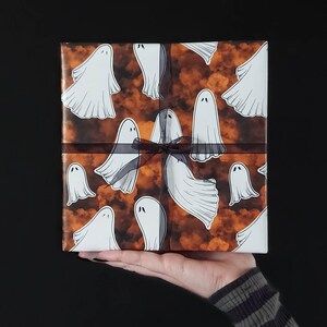 May include: Orange and white gift wrap with a pattern of ghosts. The gift is tied with a black ribbon.