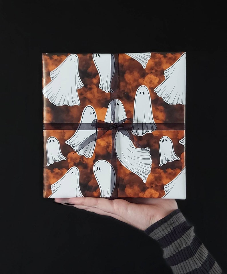 May include: Orange and white gift wrap with a pattern of ghosts. The gift is tied with a black ribbon.