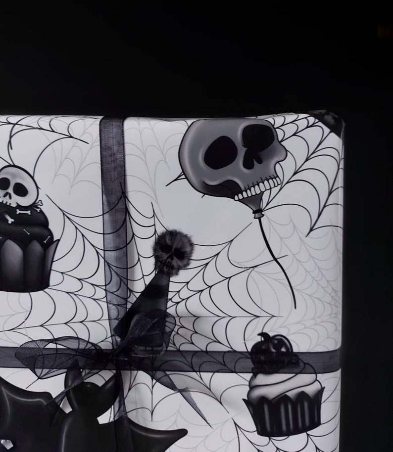 Peut inclure: Papier cadeau d'Halloween noir et blanc avec un motif de toile d'araign&eacute;e. Le papier pr&eacute;sente un ballon en forme de cr&acirc;ne, un cupcake surmont&eacute; d'un cr&acirc;ne et un cr&acirc;ne portant un chapeau de f&ecirc;te.