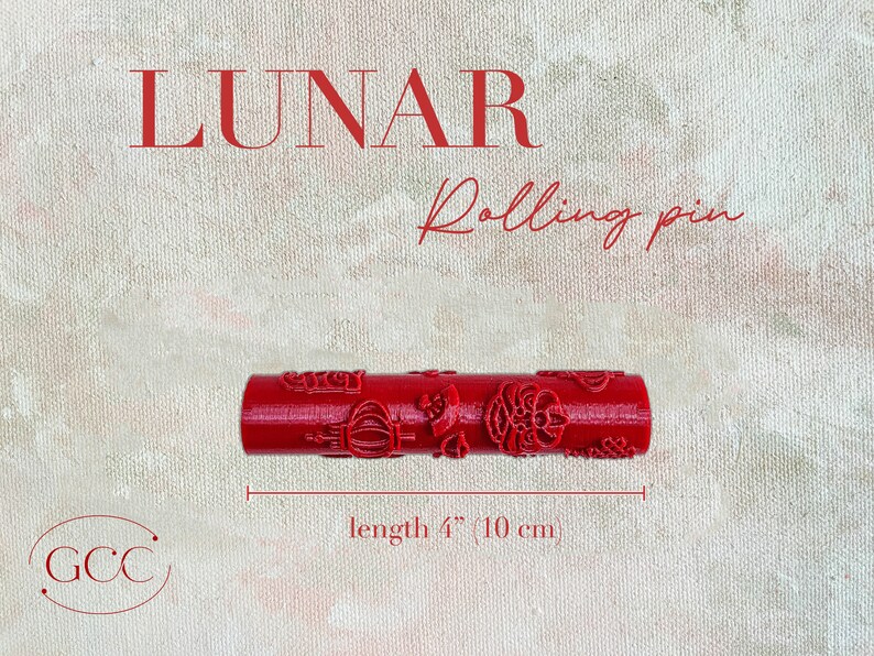 Puede incluir: Rodillo de pl&aacute;stico rojo con un dise&ntilde;o decorativo. El rodillo mide 10 cm de largo. El texto "LUNAR Rolling pin" est&aacute; por encima del rodillo. El texto "GCC" est&aacute; en un c&iacute;rculo debajo del rodillo.