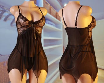 May include: Black lingerie set featuring a sheer babydoll top with lace detailing on the bust and a matching thong. The babydoll has adjustable straps and a flowing, asymmetrical hemline. The set is displayed on a mannequin.