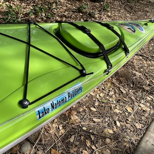 May include: A lime green kayak with black straps and a black bungee cord system. The kayak has a clear plastic strip along the edge and a sticker that says "Lake Natoma Paddlers".