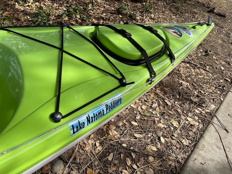 May include: A lime green kayak with black straps and a black bungee cord system. The kayak has a clear plastic strip along the edge and a sticker that says "Lake Natoma Paddlers".