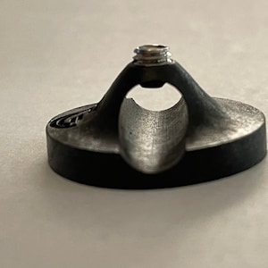 May include: A black plastic guitar strap holder with a silver screw. The holder has a curved design to fit around a guitar strap.