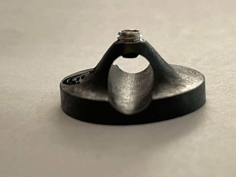 May include: A black plastic guitar strap holder with a silver screw. The holder has a curved design to fit around a guitar strap.