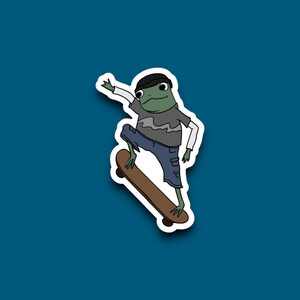 May include: A sticker featuring a cartoon frog skateboarding. The frog is green with a black beanie, gray shirt, blue shorts, and white sleeves. The skateboard is brown. The background is a solid teal color.