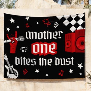 May include: Black tapestry with the text "another one bites the dust" in white gothic font. Features red graphics of a hand holding a microphone, a speaker, musical notes, stars, and a guitar. A checkered flag design is in the upper right corner.