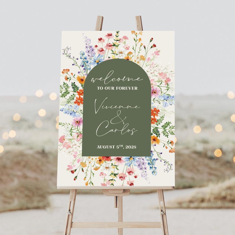 May include: A wedding welcome sign on an easel. The sign features a floral design with a green arch containing the words "welcome to our forever" and the names "Vivienne & Carlos" with the date "August 5th, 2028". The background is a cream color.