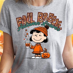 May include: A gray t-shirt with a graphic of a cartoon character holding a cup of coffee and a pumpkin. The text "Fall Breeze Autumn Leaves" is printed on the shirt.