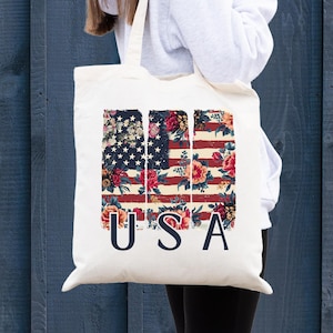 May include: A white canvas tote bag with a floral design American flag and the word "USA" printed on it.