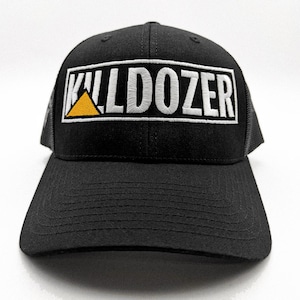 May include: Black baseball cap with a curved brim and mesh back. The front features the word "DOZER" in white embroidered letters inside a black rectangle with a yellow triangle. The hat is a trucker style.