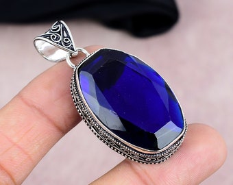 Op de afbeelding: Een zilveren hanger met een ovale, facetgeslepen, diepblauwe edelsteen. De edelsteen is gezet in een decoratieve zilveren lijst met ingewikkelde details. De hanger heeft een lus aan de bovenkant voor een ketting.