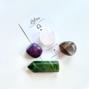 May include: A set of four crystals for the zodiac sign Libra. The crystals are a pink rose quartz, a purple amethyst, a brown sunstone, and a green jade. The card reads "Libra September 23 October 22" with the Libra symbol. The card also lists the properties of each crystal.