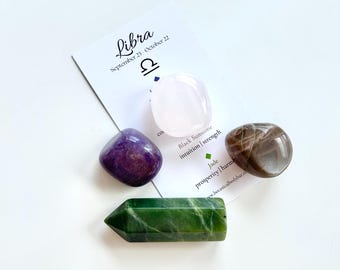 May include: A set of four crystals for the zodiac sign Libra. The crystals are a pink rose quartz, a purple amethyst, a brown sunstone, and a green jade. The card reads "Libra September 23 October 22" with the Libra symbol. The card also lists the properties of each crystal.