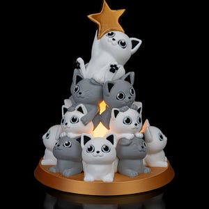 May include: A white cat figurine with a gold star on its head sits atop a stack of gray cat figurines, forming a Christmas tree shape.
