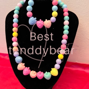 Peut inclure: Un ensemble de collier et de bracelet en perles de couleur pastel avec des perles en forme de fraise. Le collier est plus long que le bracelet et les deux sont faits de perles en plastique colorées.