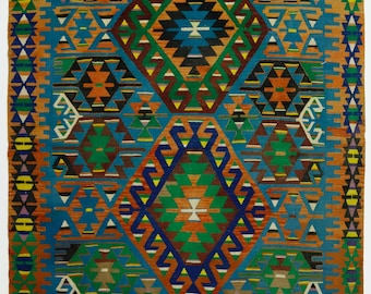 May include: A rectangular, woven rug with a geometric pattern. The rug features a central diamond design in green, blue, and orange, surrounded by smaller geometric shapes in various colors. The background is primarily blue, with orange and brown borders.
