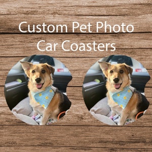 May include: Two round car coasters with a photo of a dog wearing a blue and yellow bandana sitting in a car. The coasters are made of a durable material and are designed to protect your car's interior from spills and scratches.  Custom Pet Photo Car Coasters.