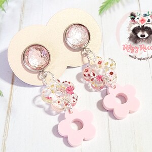 May include: Pink and white floral dangle earrings with a pink flower charm. The earrings feature a silver tone metal chain and a pink and white floral design. The earrings are handmade and have a delicate and feminine look.