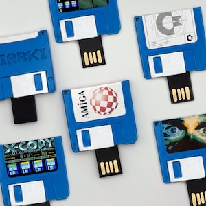 Pode incluir: Uma coleção de pen drives azuis projetados para se parecerem com disquetes de 3,5 polegadas. Cada unidade possui um conector preto e vários rótulos, incluindo X-Copy Professional, Amiga, Miarki e ilustrações gráficas de discos e olhos.
