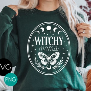 K&ouml;nnte beinhalten: Dunkelgr&uuml;nes Sweatshirt mit wei&szlig;em ovalem Design. Das Design enth&auml;lt den Text "Witchy Mama", einen Schmetterling, Halbmonde und Sterne. SVG- und PNG-Symbole befinden sich in der unteren linken Ecke.
