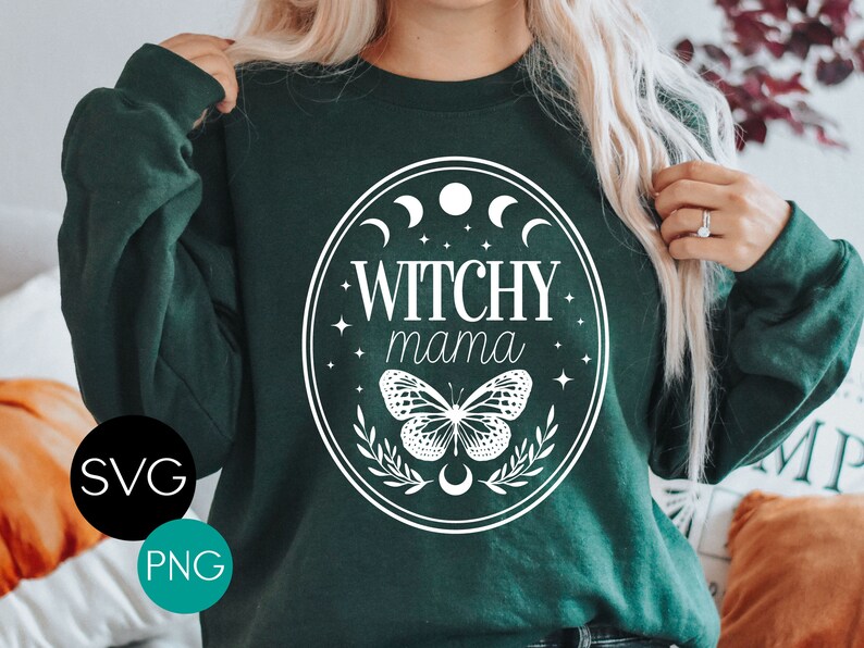K&ouml;nnte beinhalten: Dunkelgr&uuml;nes Sweatshirt mit wei&szlig;em ovalem Design. Das Design enth&auml;lt den Text "Witchy Mama", einen Schmetterling, Halbmonde und Sterne. SVG- und PNG-Symbole befinden sich in der unteren linken Ecke.