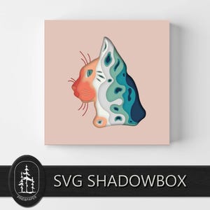 May include: A layered paper art piece featuring a cat's profile. The cat's face is a gradient of orange and white, transitioning to blue and white layers. The artwork is mounted on a light pink square.