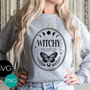 K&ouml;nnte beinhalten: Ein graues Sweatshirt mit einem schwarzen Aufdruck, der "Witchy Mama" in einem ovalen Rahmen mit Mondphasen, Sternen, einem Schmetterling und Bl&auml;ttern zeigt. Das Bild enth&auml;lt auch die Texte "SVG" und "PNG" in einem Kreis.