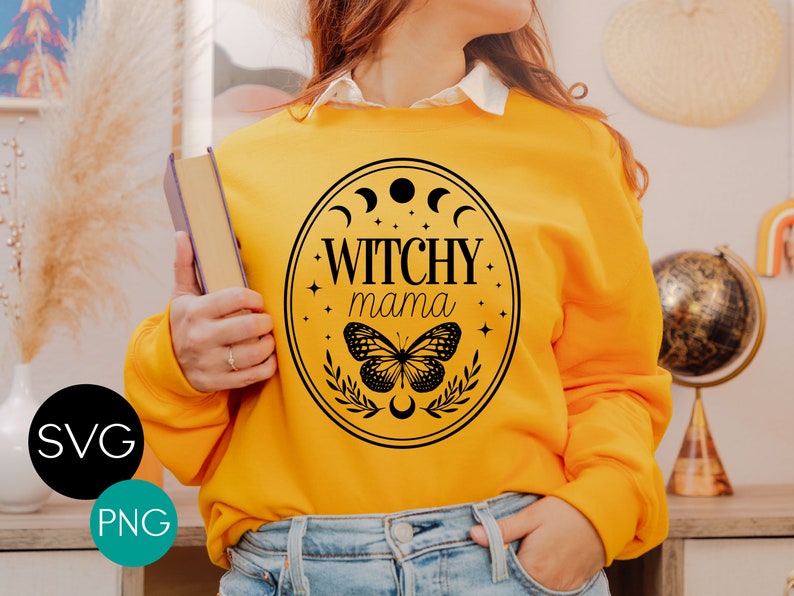 K&ouml;nnte beinhalten: Senfgelbes Sweatshirt mit schwarzem Aufdruck &bdquo;Witchy Mama&ldquo; in einem ovalen Rahmen. Der Rahmen enth&auml;lt Halbmonde, Sterne, einen Schmetterling und Bl&auml;tter. Das Bild enth&auml;lt auch SVG- und PNG-Dateityp-Symbole.