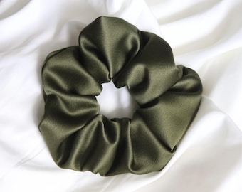 May include: A dark green satin scrunchie hair tie. The scrunchie is made of soft, silky fabric and is designed to be gentle on hair.
