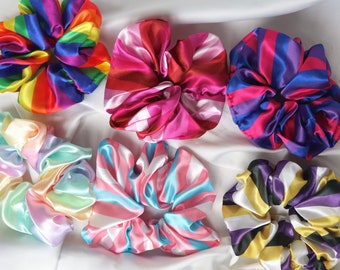 May include: Six colorful satin scrunchies with different striped patterns. The scrunchies are arranged on a white surface.