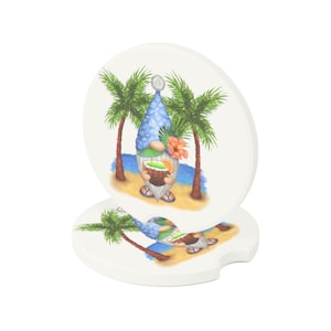 May include: A set of two round white coasters with a blue gnome holding a tropical drink in front of two palm trees on a beach. The gnome is wearing a blue hat and has a white beard.