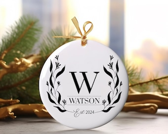 May include: White ceramic Christmas bauble featuring a black floral wreath design, the letter "W" in the centre, and the text "WATSON Est. 2024".