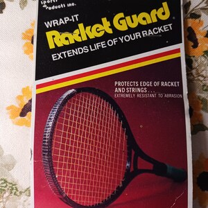 May include: A red and yellow package with the text "Racket Guard" in black and yellow letters. The text "Wrap-It" is in black letters. The package shows a tennis racket with a black handle and a red and yellow string pattern. The text "Extends Life of Your Racket" is in black letters. The text "Protects Edge of Racket and Strings... Extremely Resistant to Abrasion" is in black letters. The text "7 Feet... Long Enough for Big Rackets." is in black letters.