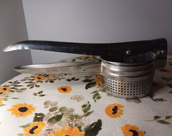 May include: A silver potato ricer with a long handle. The ricer has a perforated bowl and a lever that presses down on the potatoes.