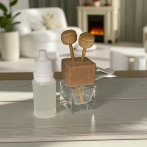 May include: A clear glass aromatherapy diffuser with a wooden top and two wooden diffuser sticks. A small, clear plastic bottle with a white cap is next to the diffuser. The items are on a light-coloured surface.