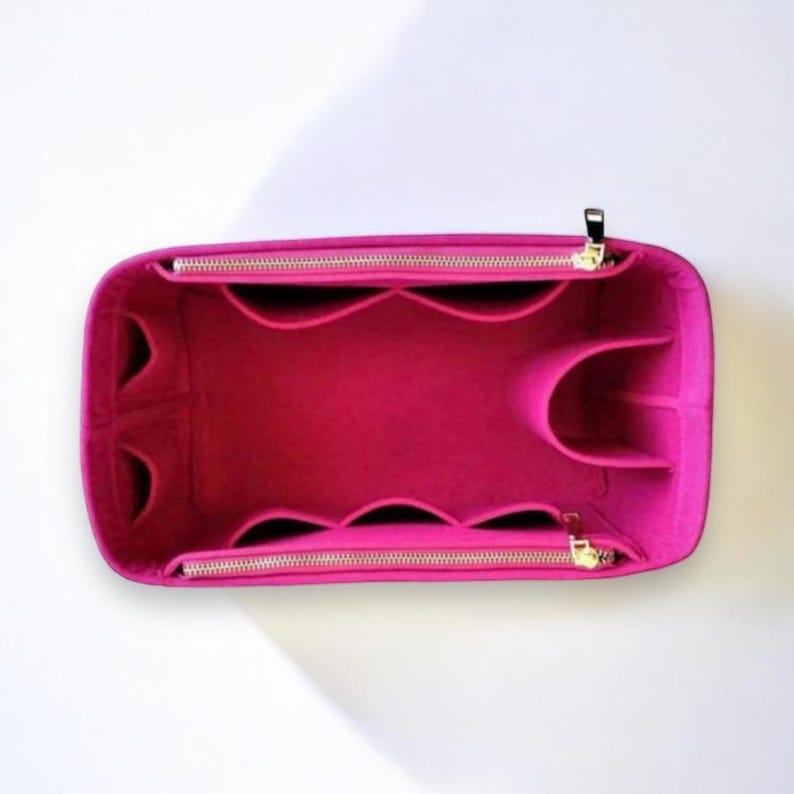 Puede incluir: Un organizador de bolso de fieltro rosa con m&uacute;ltiples compartimentos y cierre de cremallera. El organizador est&aacute; dise&ntilde;ado para caber dentro de un bolso m&aacute;s grande y ayudar a mantenerlo organizado.