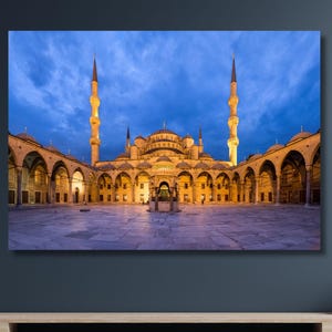 May include: A canvas print of the Blue Mosque in Istanbul, Turkey, at dusk. The mosque is illuminated with warm lighting, set against a deep blue sky. Two tall minarets flank the central dome.