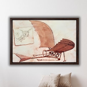 Puede incluir: Impresión enmarcada de un boceto de Leonardo da Vinci de una máquina voladora. La obra de arte presenta un dibujo en tonos sepia de la máquina con estructuras en forma de ala y un pequeño boceto de una figura. El marco es marrón oscuro.