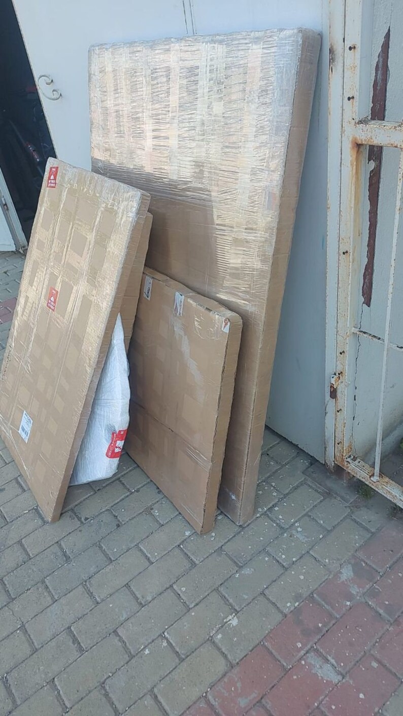 May include: Three cardboard boxes stacked on top of each other. The boxes are wrapped in clear plastic and have a brown and white pattern. The boxes are sitting on a gray brick surface.