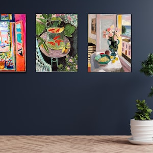 May include: Three paintings in colorful, impressionistic styles. The leftmost painting shows a window with an open view of a beach and sailboats. The middle painting shows a bowl of goldfish on a table with green plants. The rightmost painting shows a vase of pink flowers on a table with a view of a beach and a palm tree.