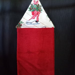 K&ouml;nnte beinhalten: Rotes K&uuml;chentuch mit einer wei&szlig;en und gr&uuml;nen Schleife aus Weihnachtsstoff. Die Schleife zeigt einen wei&szlig;en Schlittschuh mit einer roten Schleife und Stechpalme.