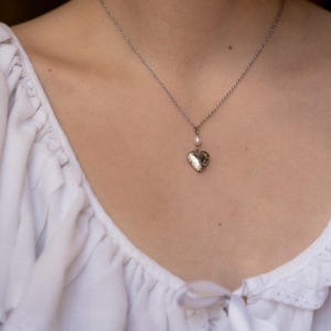 May include: A silver chain necklace with a heart-shaped locket and a single pearl charm.