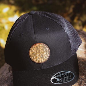 May include: Black mesh and twill baseball cap with a brown leather patch featuring a wave pattern. The cap has a black Flexfit Tech label with the text "110 One Ten".